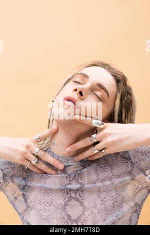 Tätowierte nicht-binäre Person mit silbernem Zubehör, das den Hals berührt, isoliert auf gelbem Stockbild Stockfoto