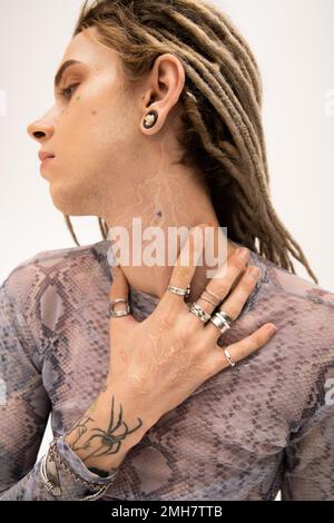 Seitenansicht einer jungen tätowierten schwulen Person, die den Hals berührt, isoliert auf weißem Stockbild Stockfoto