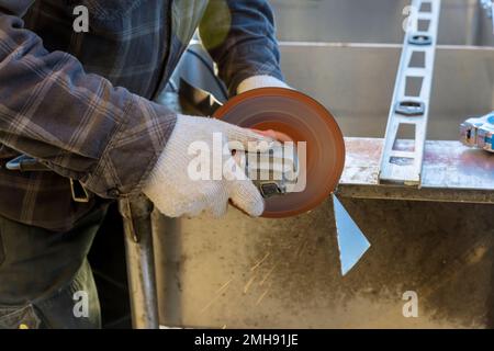 Der Arbeiter verwendet eine Schleifmaschine, um Metall mit Funken zu schneiden, während er das Bügeleisen mit der Schleifmaschine schleift Stockfoto