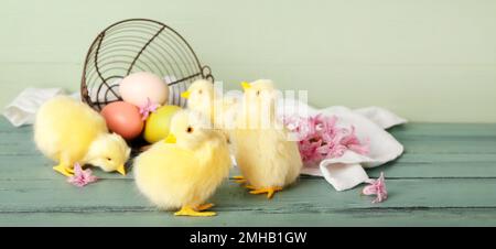 Niedliche Hühner, umgedrehtes Korb mit Ostereiern und Blumen auf Holztisch Stockfoto