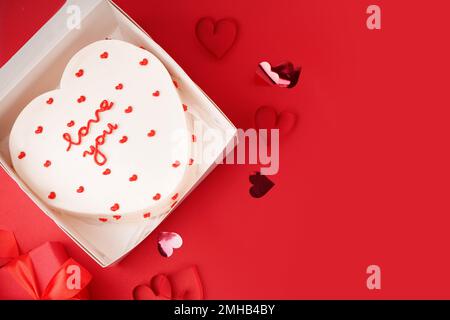 Geöffnete Schachtel mit herzförmigem Bento-Kuchen auf rotem Hintergrund. Valentinstag-Feier Stockfoto