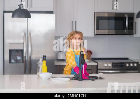 Wasch- und Reinigungskonzept. Kinderhilfe im Haushalt, Geschirr abwischen in der Küche. Kinderbetreuung. Der kleine Junge fegt und putzt Stockfoto