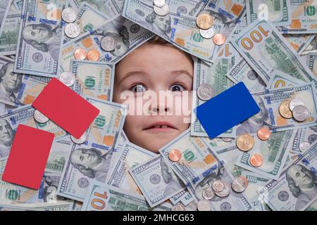 Lustiges Kind mit lustigem Gesicht und Geld. Ein Kind, das mit schockierten Augen aus Dollarscheinen guckt. Geld-Hintergrund. Einkaufs- und Finanzkonzept Stockfoto