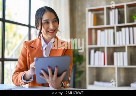 Charmante asiatische Geschäftsfrau oder CEO-Frau, die ihr digitales Tablet zur Verwaltung ihrer geschäftlichen Aufgaben im Büro verwendet. Stockfoto