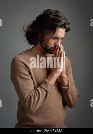 Was soll ich tun? Studioaufnahme eines gutaussehenden jungen Mannes, der vor grauem Hintergrund betet. Stockfoto