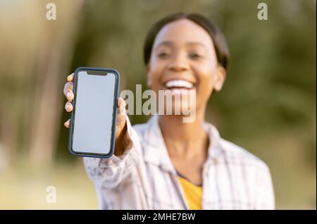 Mockup, Smartphone und schwarze Frau in der Natur oder Park mit fröhlichem Porträt für die mobile App oder Produktplatzierung. Afrikanische Person, Handheld-Telefon und Stockfoto