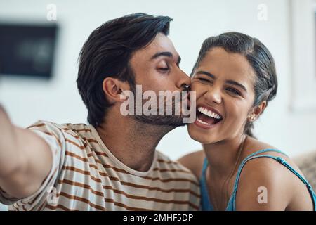 Liebe macht Zeit zum Spaß. Porträt eines glücklichen jungen Paares, das zu Hause für ein Selfie posiert. Stockfoto