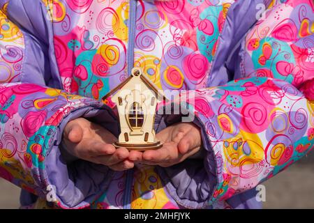 Die Kinderhand hält ein kleines Holzhaus auf einem verschwommenen Hintergrund Stockfoto