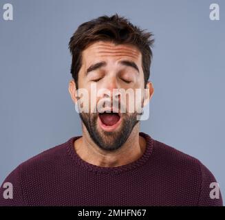 Dieser Tag ist noch vorbei. Studioaufnahme eines gutaussehenden jungen Mannes, der vor grauem Hintergrund gähnt. Stockfoto