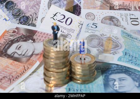 Aktenfoto vom 11. Oktober 09/18 von Modellen eines Mannes und einer Frau, die auf einem Haufen Münzen und Banknoten stehen. Neue Forschungsergebnisse deuten darauf hin, dass die Bezahlung von Arbeitern in der Stadt, wie etwa im Finanz- und Versicherungssektor, mehr als dreimal schneller gestiegen ist als die Bezahlung von Krankenschwestern, Sanitätern und Hebammen seit 2008. Stockfoto