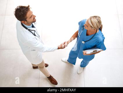 Willkommen in unserem Team. Im Foyer des Krankenhauses schüttelten zwei Ärzte die Hände in einem hohen Winkel. Stockfoto