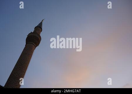 Das Bild zeigt ein hohes, schlankes Minarett mit einer spitzen Spitze gegen einen verlaufenden Himmel bei Sonnenauf- oder -Untergang. Stockfoto