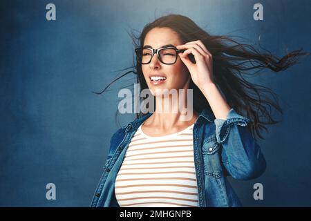 Etwas großes kommt auf uns zu. Studiofoto einer jungen Frau, die vor blauem Hintergrund Luft ins Gesicht geblasen hat. Stockfoto