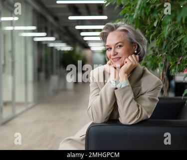 Attraktive, reife Frau, die auf dem Sofa in der Lobby sitzt. Stockfoto