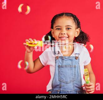 Kleines Mädchen, Porträt oder Blasen spielen auf isoliertem rotem Hintergrund in Hand-Augen-Koordination, Kinderaktivität oder lustiges Spiel. Lächeln, glücklich oder Kind und Stockfoto