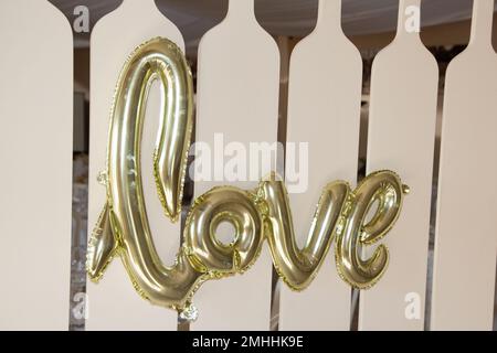 Liebesworttext aus goldenem aufblasbarem Ballon auf Wandhintergrund im Konzept der Romantik des Valentinstages Stockfoto