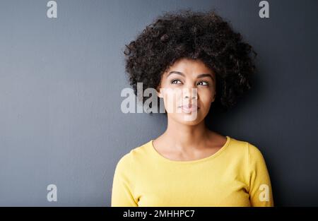 Sie hat viel um die Ohren. Studioaufnahme einer attraktiven jungen Frau, die aufmerksam aussieht, während sie vor grauem Hintergrund posiert. Stockfoto