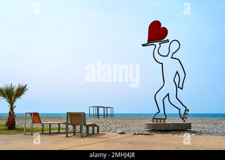 Eine Skulptur in Form eines Kellners auf Rollen, der ein Herz auf einem Tablett trägt. In der Nähe des Cafés am Strand. Batumi, Georgia - 03.23.2021 Stockfoto