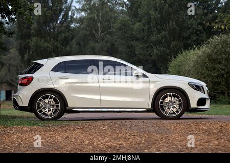 Modernes weißes Auto, das im Parkhintergrund fährt, luxuriöse Stadtfahrzeugtapete Stockfoto