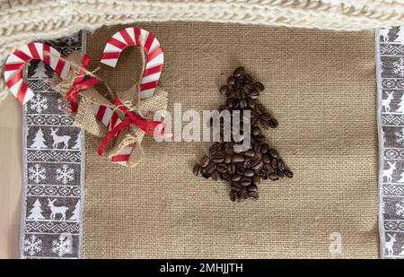 Ein Blick von oben auf zwei dekorative Zuckerstangen und einen Weihnachtsbaum aus Kaffeebohnen über einer Jutetischdecke. Stockfoto