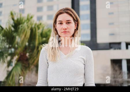 Nahaufnahme eines Porträts einer blonden weißen jungen Frau, die ernsthaft vor die Kamera schaut. Hübsches Teenager-Mädchen, das mit trauriger Einstellung nach vorne starrt. Hochwertige 4K-Aufnahmen Stockfoto