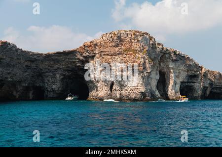 Touristen auf der Yacht erkunden natürliche Steinbögen und Höhlen. Küstenlandschaft der Insel Comino, Malta Stockfoto