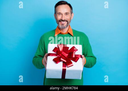 Foto eines erwachsenen, gutaussehenden Mannes, der eine große geschenkbox in der Hand hält. Tragen Sie trendige grüne Kleidung, isoliert auf blauem Hintergrund Stockfoto