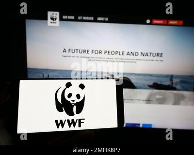 Person, die ein Mobiltelefon mit dem Logo des World Wide Fund for Nature Inc. Besitzt (WWF) auf dem Bildschirm vor der Webseite. Konzentrieren Sie sich auf das Display des Telefons. Stockfoto
