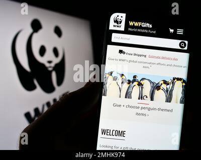Person, die ein Mobiltelefon mit der Website des World Wide Fund for Nature Inc. Besitzt (WWF) auf dem Bildschirm vor dem Logo. Konzentrieren Sie sich auf die Mitte des Telefondisplays. Stockfoto