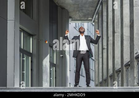 afroamerikanischer Boss feiert Sieg und Erfolg, Geschäftsmann tanzt auf der Treppe des modernen Bürogebäudes. Stockfoto