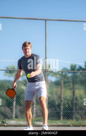 Ein Mann spielt Pickleball-Spiel, schlägt Pickleball-gelben Ball mit Paddel, Outdoor-Sport-Freizeitaktivitäten. Stockfoto