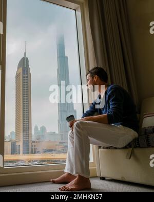 Depressive Männer sitzen in einem Zimmer eines Bürogebäudes mit Blick auf Dubai Vereinigte Arabische Emirate. Stockfoto