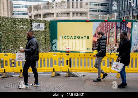 Mittagszeit gehen Londoner mit den gleichen Lunchtaschen vorbei an einer Industrielandschaft des Bauunternehmers Robert McAlpine vom Bau von „One Broadgate“ Umbau von 1 Broadgate in der Nähe der Liverpool Street Station in der City of London, dem Finanzviertel der Hauptstadt, am 26. Januar 2023 in London, England. Stockfoto