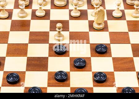 Spielen nach unterschiedlichen Regeln auf einem Spielbrett - schwarze und weiße Schachfiguren auf einem Holzschachbrett, Beginn des Schachspiel (Schwerpunkt Stockfoto