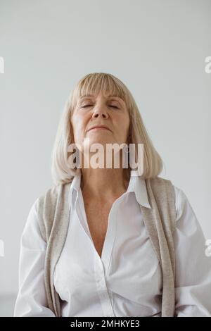 Studioporträt einer grauhaarigen Seniorin. Er sitzt traumhaft und meditiert. Stockfoto