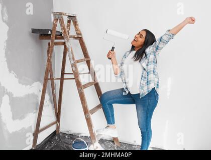 Weitwinkel einer jungen Indianerin, die mit Malerwalze singt, während sie Wand malt Stockfoto