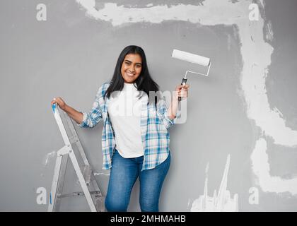 Junge Indianerin posiert mit Pinsel-Walze und macht sich bereit, Wände zu streichen Stockfoto