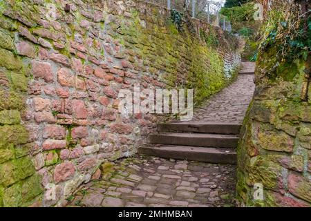 Ein typischer Abschnitt des Schlangenweges, ein schmaler kopfsteingepflasterter Fußweg mit Stufen, flankiert von roten Sandsteinwänden, die sich im Zickzack hinaufbewegen... Stockfoto