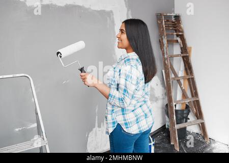 Eine junge indische Frau bereitet sich darauf vor, während eines Heimwerkerprojekts eine Wand zu streichen Stockfoto
