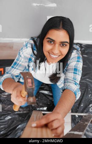 Eine attraktive junge Indianerin hämmert einen Nagel in das Heimwerkerhaus Stockfoto