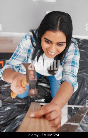 Eine attraktive junge Indianerin hämmert einen Nagel in das Heimwerkerhaus Stockfoto