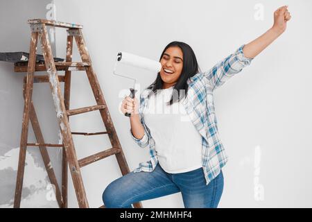 Nahaufnahme einer jungen Frau, die singt und tanzt, während sie Heimwerker streicht Stockfoto