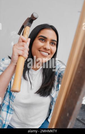 Eine attraktive junge Indianerin hämmert einen Nagel in das Heimwerkerhaus Stockfoto