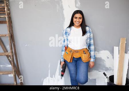 Eine attraktive junge indische Frau lehnt sich an die Wand und macht Heimwerkerrenovierungen Stockfoto