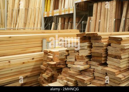 Holzstapel auf Lagerregalen. Holzbretter, -Futter und -Platten für Bauarbeiten werden im Baumarkt präsentiert. Stockfoto