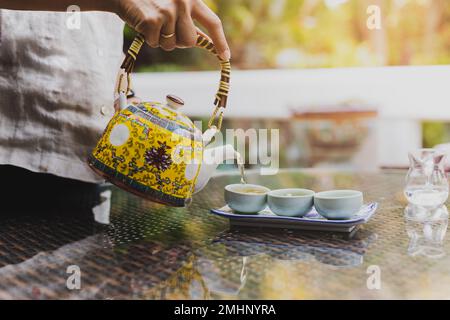 Frau schüttet von Hand Kräutertee in einen Topf auf natürlich verschwommenem Hintergrund. Stockfoto