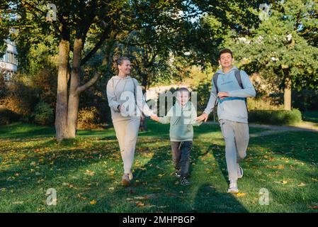 Eine familienmutter und 2 Söhne haben Spaß, Rennen im Park und springen. Söhne, Kinder, mom, Lauf, Spiel, Freuen Sie sich, genießen Sie die Natur im Sommer. Familie Stockfoto