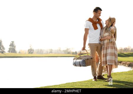 Ein junges Paar mit Picknickkorb in der Nähe des Sees an sonnigen Tagen Stockfoto