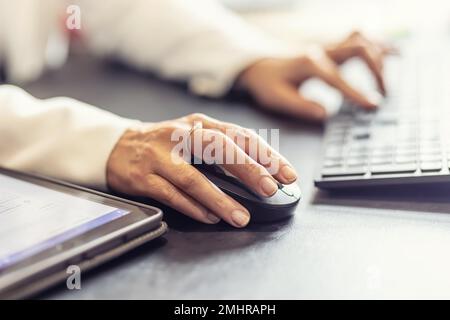 Hände einer Geschäftsfrau, die Computermaus und Tastatur im Büro hält. Stockfoto