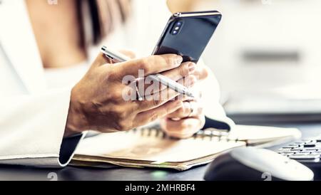 Hände einer weiblichen Führungskraft mit einem Mobiltelefon, Kommunikation mit Kollegen während der Arbeitszeit, Senden von Nachrichten oder Empfangen von Arbeitsinformationen. Stockfoto